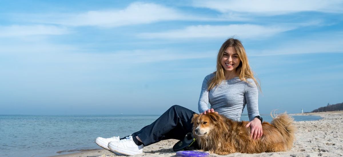 Woman enjoying a sunny day on Kołobrzeg beach with her dog, capturing the essence of leisure and companionship.